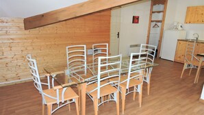 A dining area with a glass table and white chairs, wooden flooring, and a wooden ceiling.