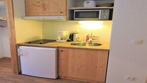 A compact kitchen with wooden cabinets, a microwave, a coffee maker, and a sink.