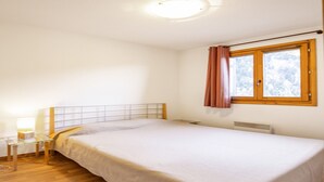 A bedroom with a single bed, a bedside table with a lamp, a window with curtains, and a radiator.