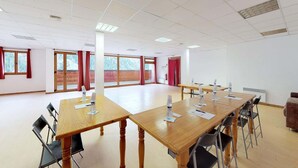 Un salón de conferencias con una mesa grande, sillas y ventanas con cortinas rojas.