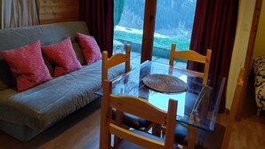 Una sala de estar acogedora con un sofá gris, almohadas rojas y una mesa de comedor de cristal con sillas de madera.
