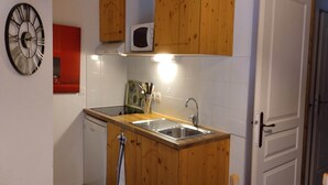 Una cocina compacta con muebles de madera, microondas integrado, lavavajillas y un lavabo.
