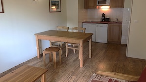 Un comedor con una mesa y sillas de madera, una pequeña cocina con microondas y lavavajillas, y una lámpara en la pared.