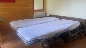 Una habitación con dos camas individuales, paredes de madera, techo blanco y un objeto rojo a la izquierda.