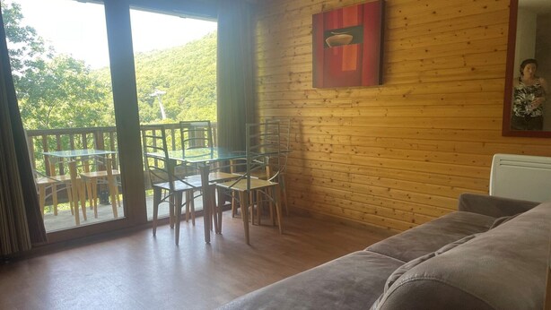 Una habitación con detalles de madera, una puerta de vidrio que da a un espacio exterior con mesas y sillas, y un sofá gris.