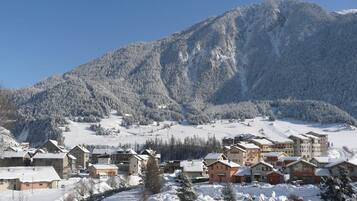 Un pueblo cubierto de nieve en la montaña con edificios de estilo chalete tradicional, una pista de esquí y un cielo azul despejado.
