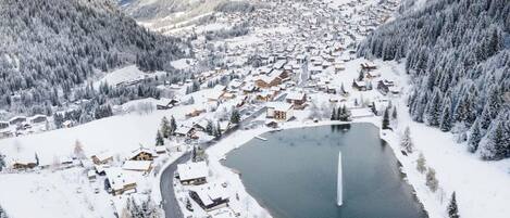 A snow-covered village with a central lake, surrounded by forested mountains.
