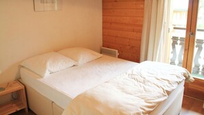 A bedroom with a wooden floor, a bed with white bedding, a nightstand, and a window with a view of the outside.