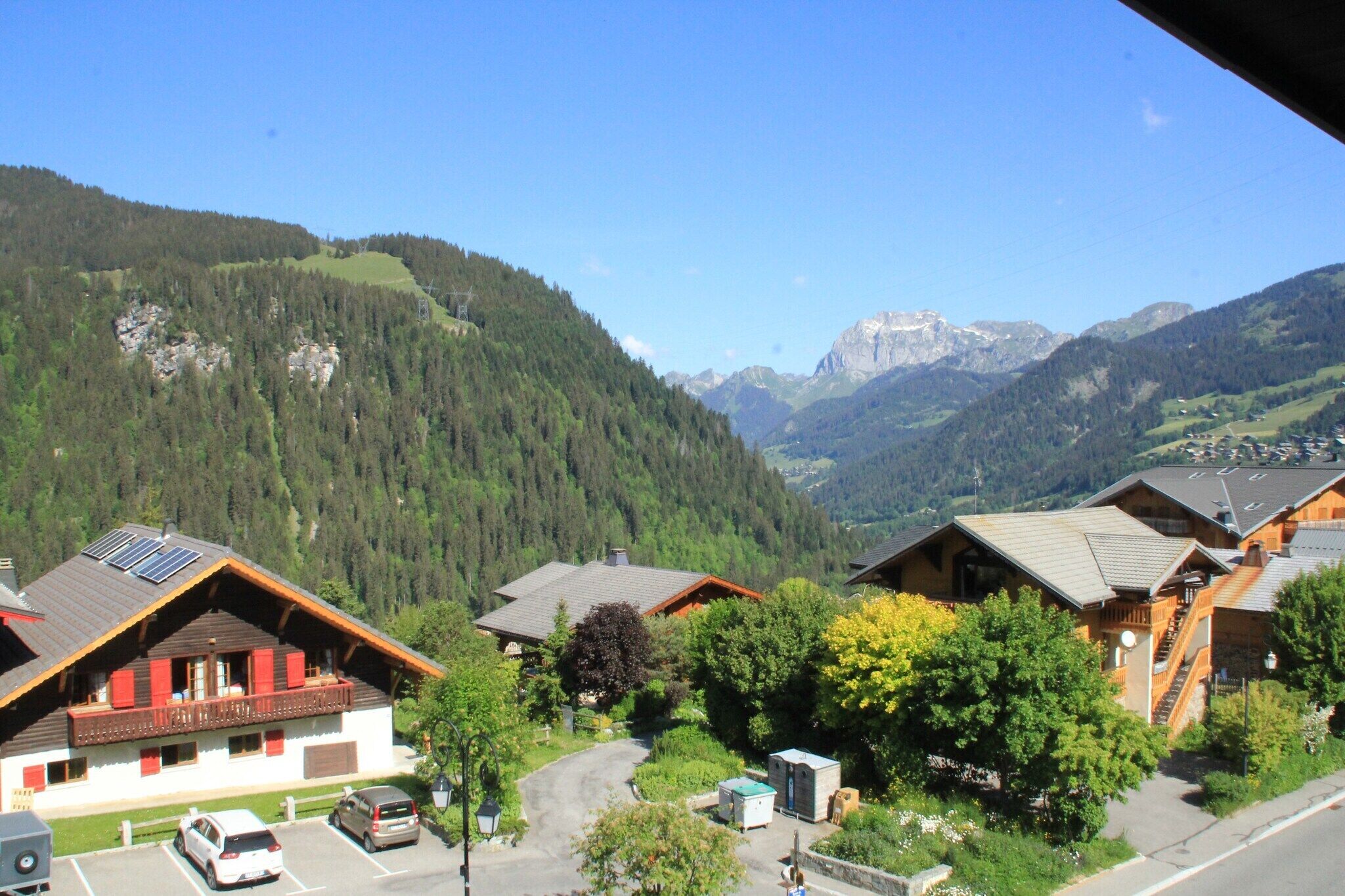A mountain village with traditional wooden houses, a paved road, and a clear view of the surrounding mountains.