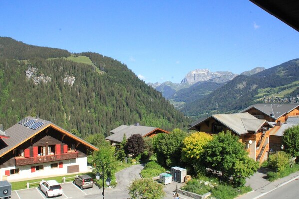 A mountain village with traditional wooden houses, a paved road, and a clear view of the surrounding mountains.