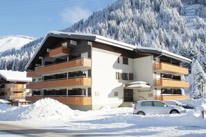 Un hôtel à plusieurs étages doté de balcons, une station de ski en arrière-plan et un paysage enneigé.