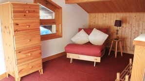 A bedroom with a wooden dresser, a bed with red bedding, a window, and a lamp. - Val Pierre apartment for 8 people (Châtel)