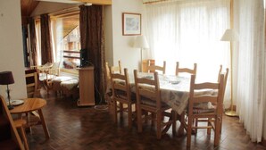 A dining area with a wooden table and chairs, a lamp, and a view of a staircase leading to another room. - Val Pierre apartment for 8 people (Châtel)