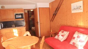 Ett kompakt bostadsutrymme med ett litet kök, en matplats och en röd soffa med mönstrade kuddar.