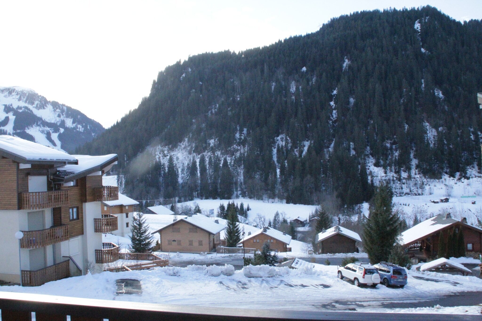A snow-covered mountain village with wooden houses and a modern building with balconies.