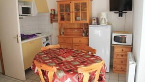 A compact kitchen with a dining table, wooden cabinets, a microwave, and a television. - Jonquilles apartment for 4 people (Châtel)
