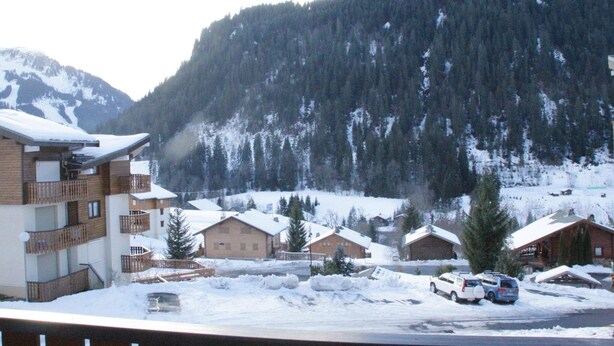 A snow-covered mountain village with wooden buildings and a parking area. - Jonquilles apartment for 4 people (Châtel)