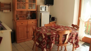 A compact kitchen with wooden cabinets, a microwave, a refrigerator, and a dining table with chairs. - Jonquilles apartment for 4 people (Châtel)