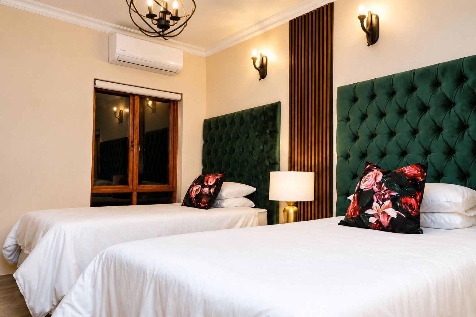 A hotel room with two beds, a large window, a green upholstered headboard, and a wall-mounted air conditioner.