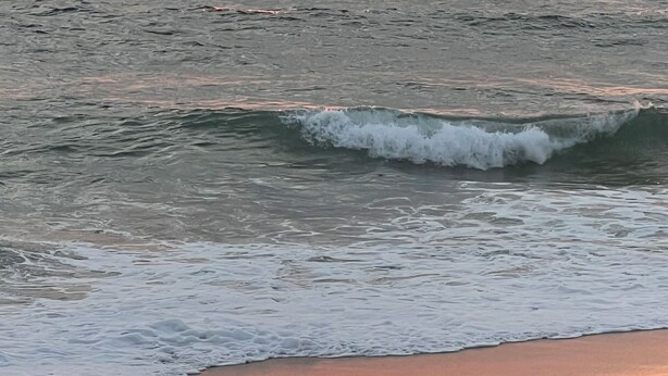 Um pôr do sol sobre o oceano com ondas se aproximando da costa.