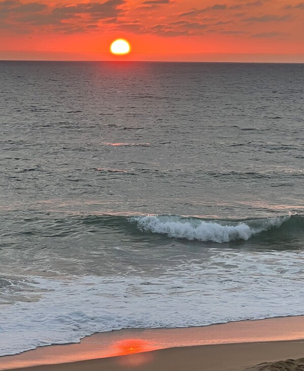 Een zonsondergang boven de oceaan, met golven die de kust naderen.