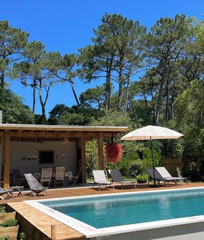 Un espace piscine avec des chaises longues et une pergola dotée d’un parasol.
