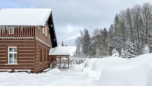 Una cabaña de madera con techo nevado y un porche de madera.