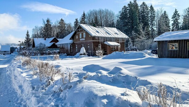 Una cabaña de madera con techo de metal, rodeada de nieve en el suelo y entre árboles.