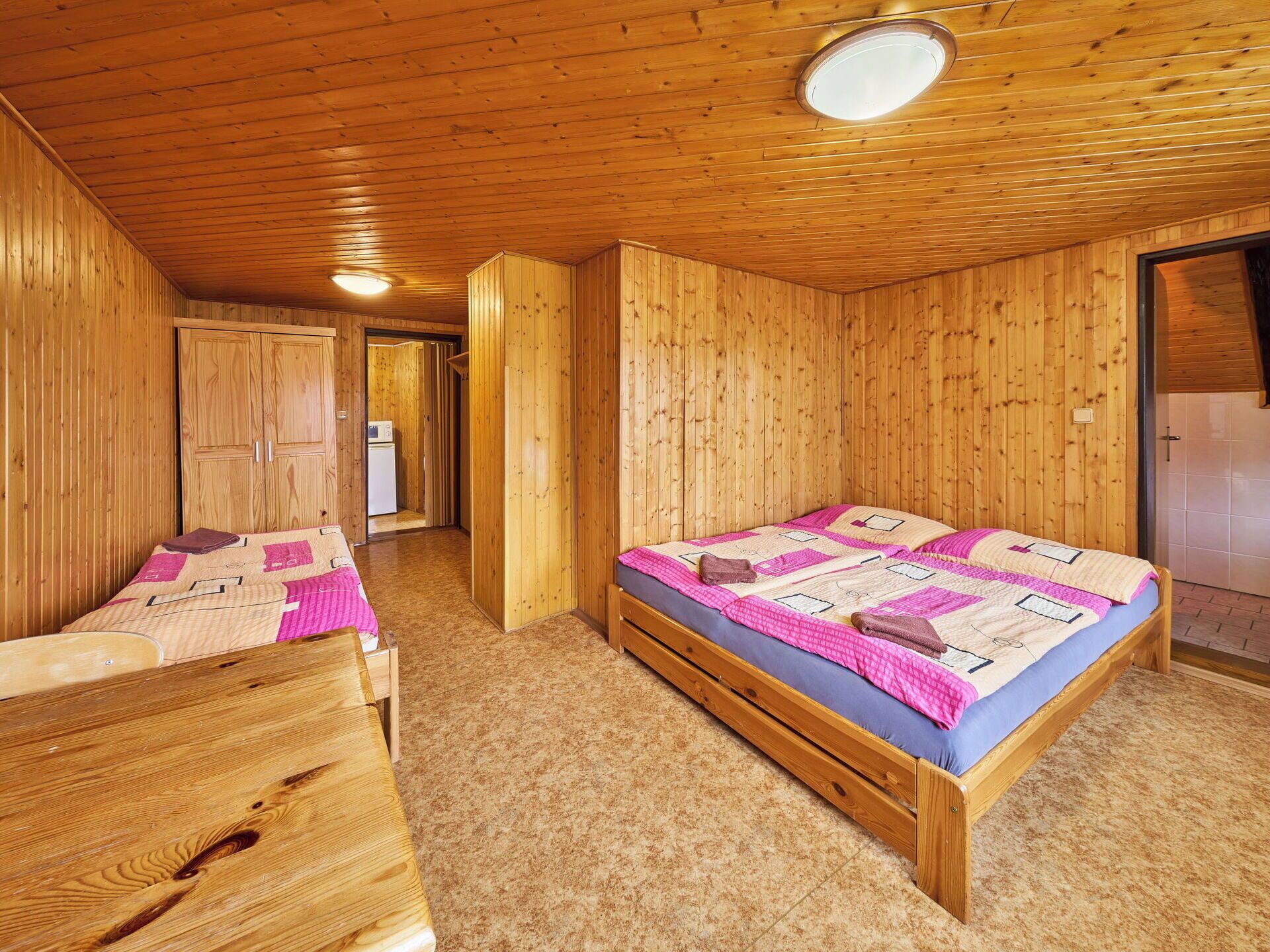 Quarto de cabana de madeira com uma cama, um banco de madeira e uma porta que dá para outro cômodo.