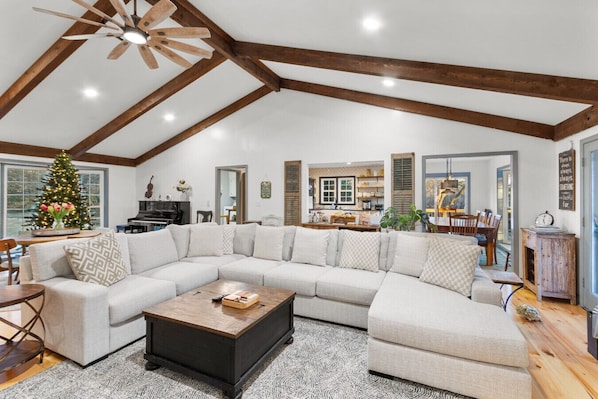 Un salon spacieux avec un grand canapé d’angle, une table basse en bois et un ventilateur de plafond.