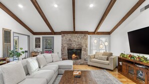 Una sala de estar con chimenea de piedra, vigas de madera, sofá modular, una mesa de centro y un televisor.