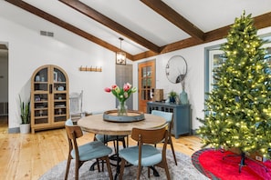 Un coin repas avec une table ronde en bois, des chaises, un vase avec des fleurs et un sapin de Noël.