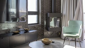 Un salon moderne avec un mur en briques, un téléviseur à écran plat fixé au mur, une table basse ronde, un fauteuil vert et une cheminée.
