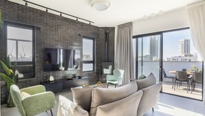 Un salon moderne avec un mur en briques, une grande fenêtre, un canapé, un téléviseur et un balcon offrant une vue sur les immebles.