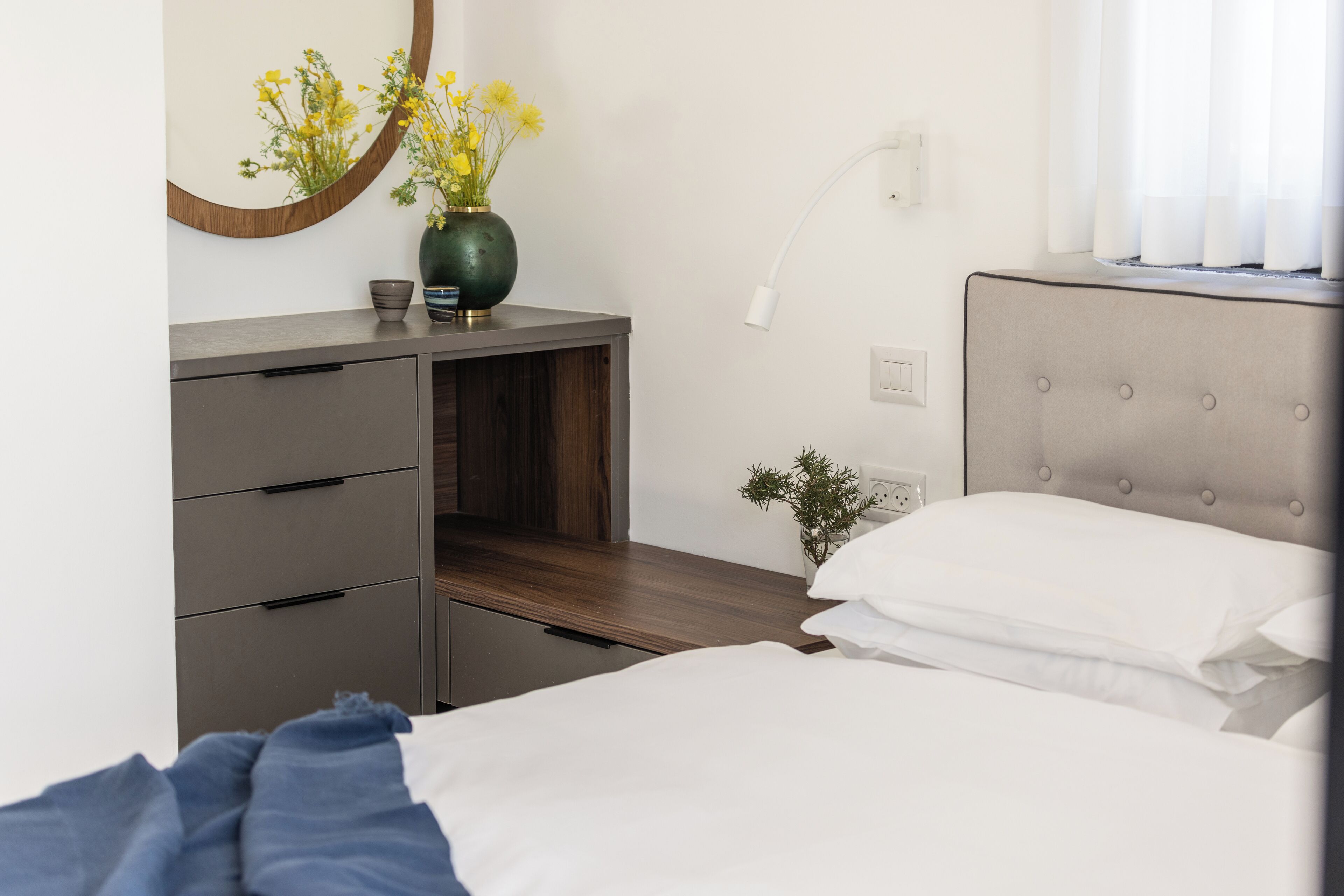 A bedroom with a bed, bedside table, dresser, mirror, and a small plant.