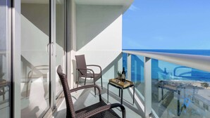 Ein Balkon mit Korbstühlen, einem kleinen Tisch mit Flasche und Glas sowie Blick auf Strand und Meer.