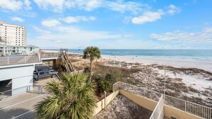 A beach view from a balcony with a parking area and a building in the background. - Clearwater 2A (Gulf Shores)