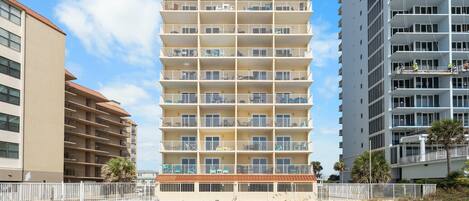 A multi-story hotel with balconies, a beach view, and a fenced walkway.