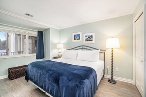 A bedroom with a bed, a nightstand, a lamp, and a window with curtains. - Beachside 214 Luxury Condo on East Grand Traverse Bay (Traverse City)