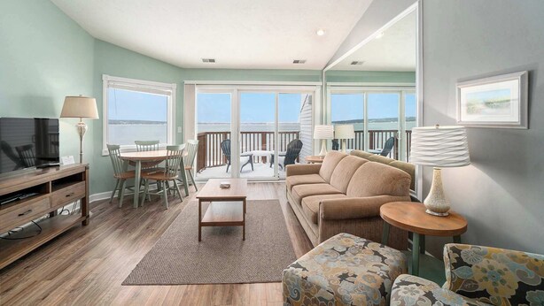 A living room with a sofa, chairs, a coffee table, and a TV. There is a balcony with a railing and a view of the water. - Beachside 325 Waterfront Condo (Traverse City)