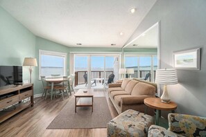A living room with a sofa, chairs, a coffee table, and a TV. There is a balcony with a railing and a view of the water. - Beachside 325 Waterfront Condo (Traverse City)