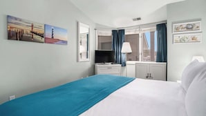 A hotel room with a bed, a desk, a television, and a window with curtains. - Beachside 325 Waterfront Condo (Traverse City)