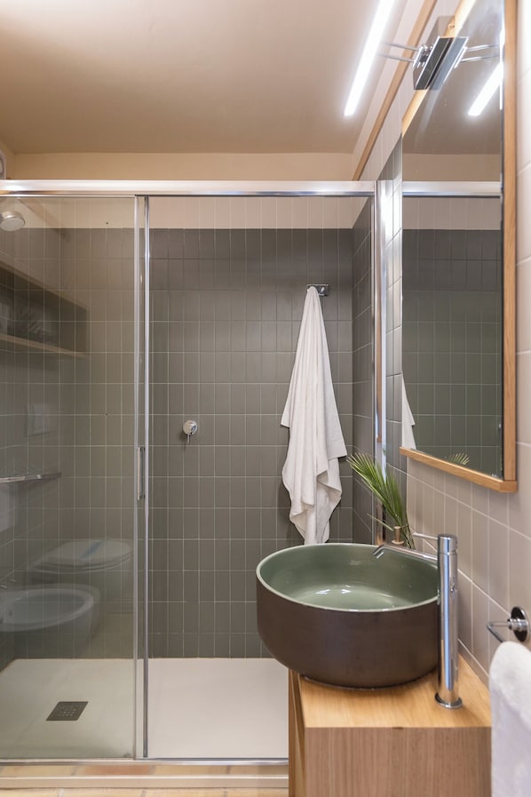 A modern bathroom with a glass-enclosed shower, a large vessel sink, and a mirror.