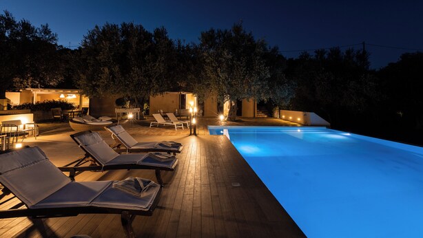 Zona junto a la piscina con sillones de descanso y una piscina por la noche.