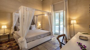 Un dormitorio con cama con dosel, mesita de noche con lámpara, una silla y vistas al exterior a través de una ventana.