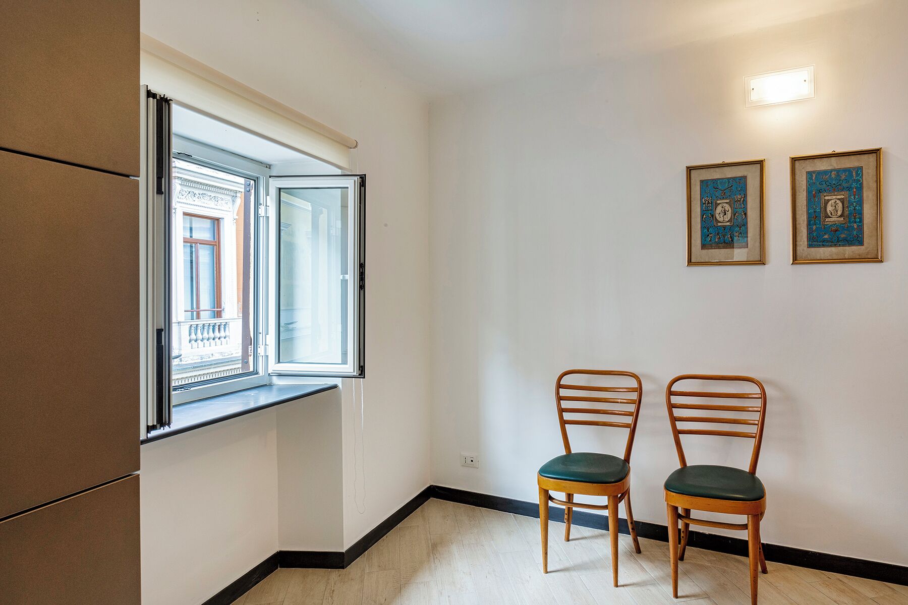 Une pièce avec une fenêtre, deux chaises en bois et deux tableaux encadrés accrochés au mur.