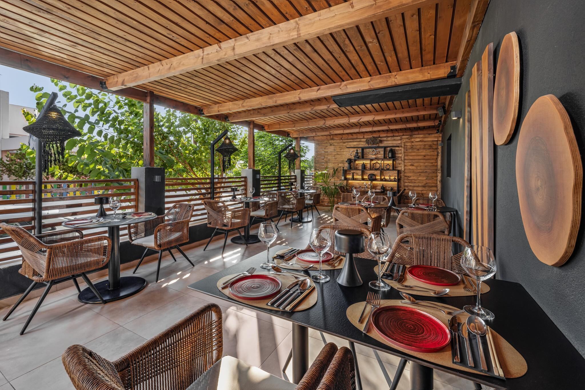 Un área de comedor al aire libre con mesas y sillas de madera, rodeada por una pérgola de madera.