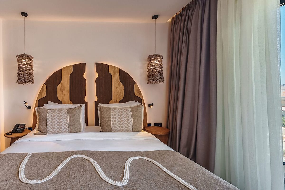 A modern hotel room with a large bed, two bedside tables, a sofa, and a unique wooden headboard design.