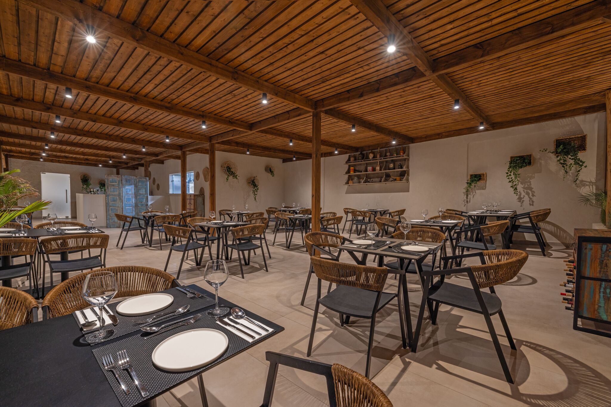 Un comedor amplio con vigas de madera en el techo, sillas de mimbre y mesas dispuestas para comer.