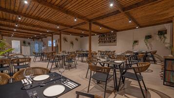 Un comedor amplio con vigas de madera en el techo, sillas de mimbre y mesas dispuestas para comer.